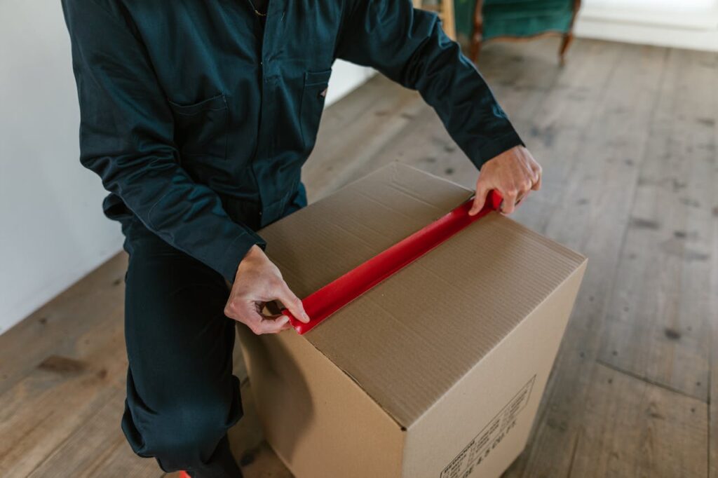 pexels-photo-7464661 A Man Sealing a Cardboard Box With Masking Tape